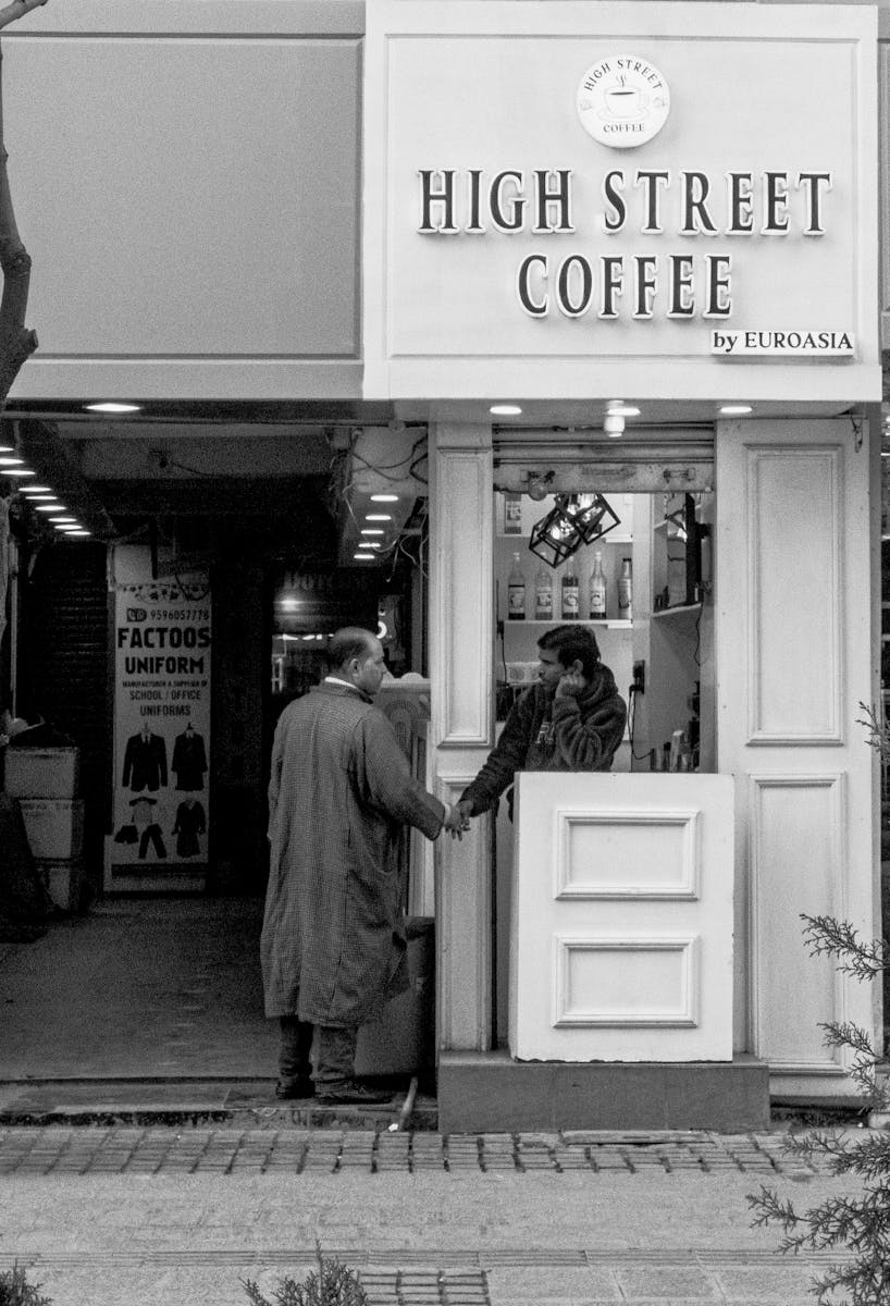 A man and a woman exchange a handshake at a coffee stand in monochrome.