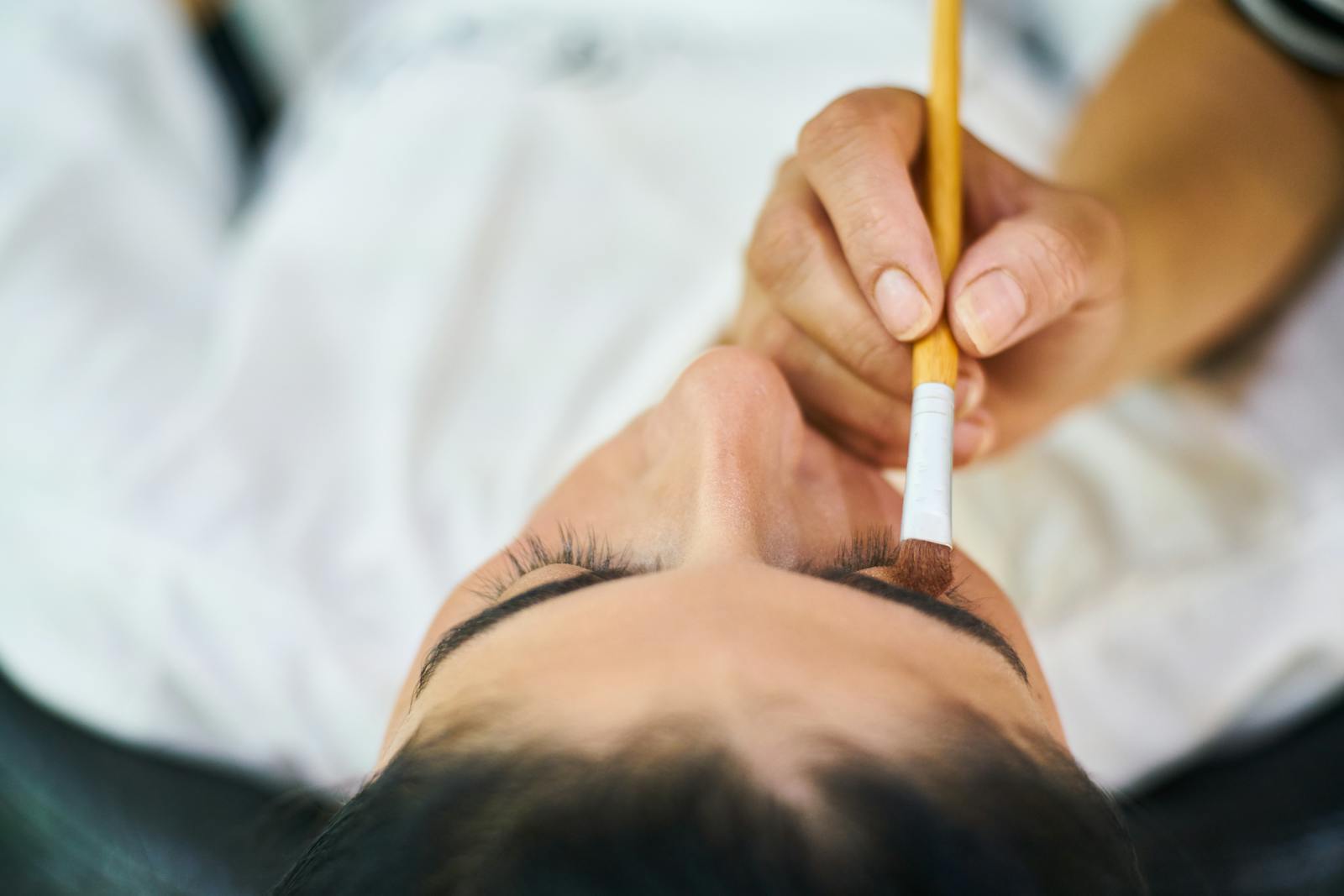 A detailed close-up of a hand applying eye shadow with a brush on a woman's eyelid.