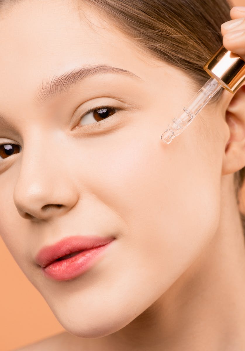 A woman applying serum with a dropper to her face for skincare routine.