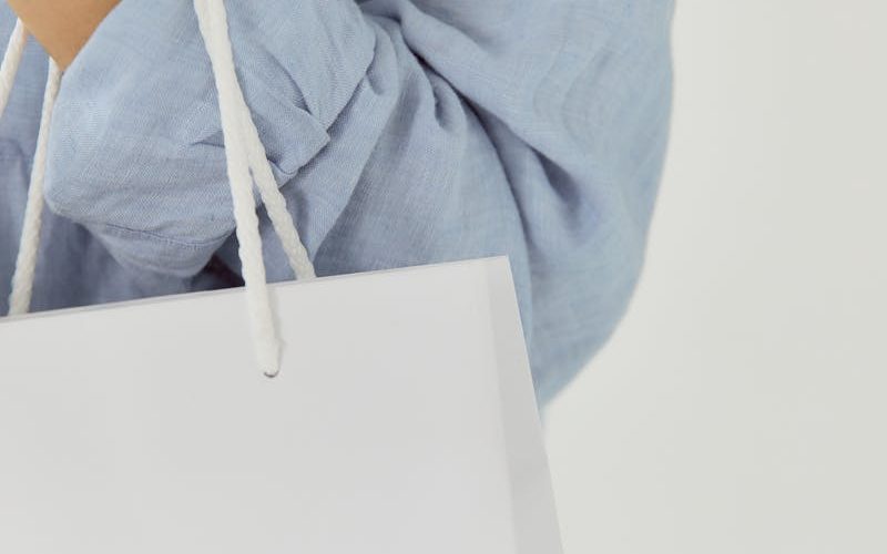 Close-up of a white shopping bag held by a person wearing a blue shirt.